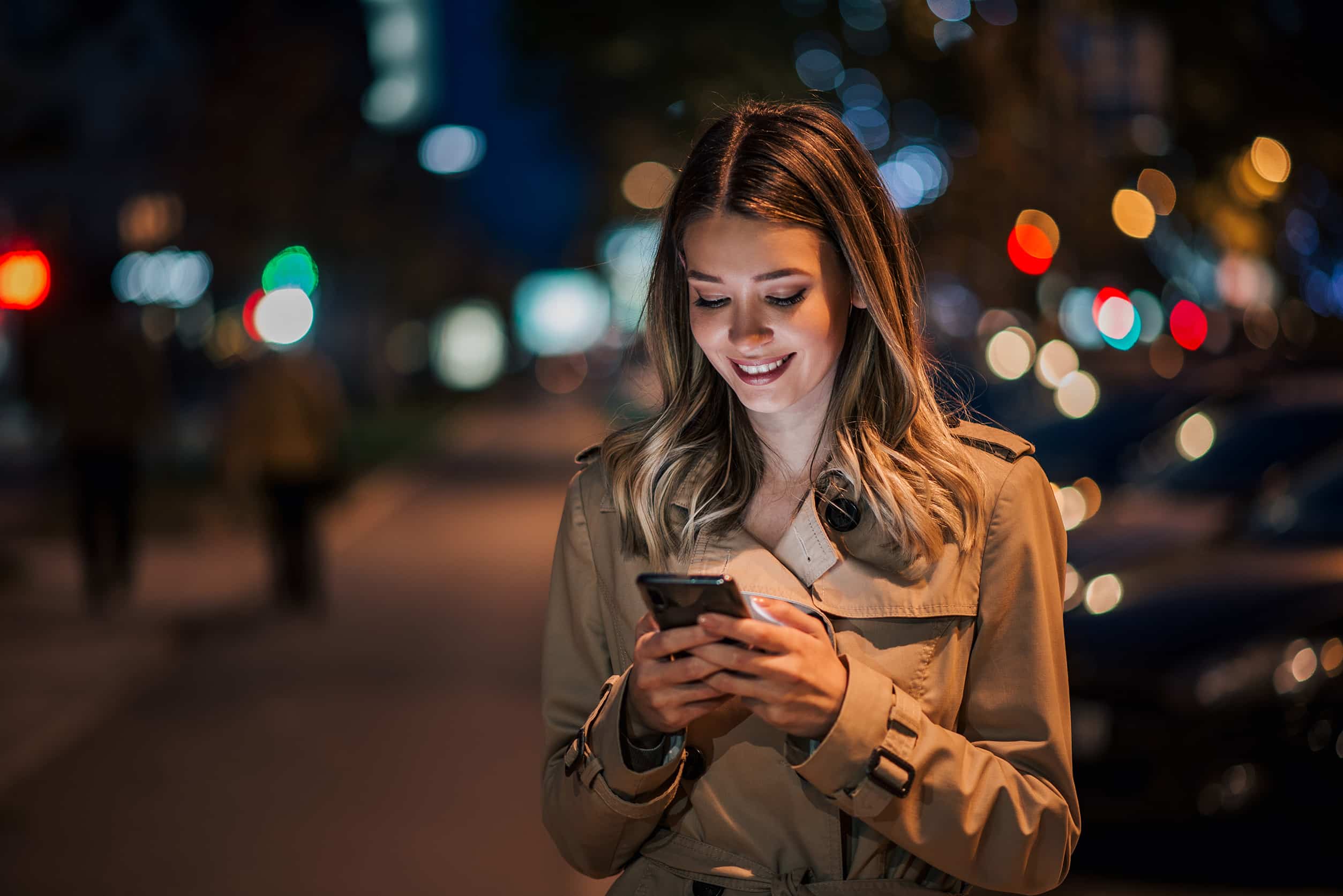 Portrait of a smiling young woman using smart phone at night.