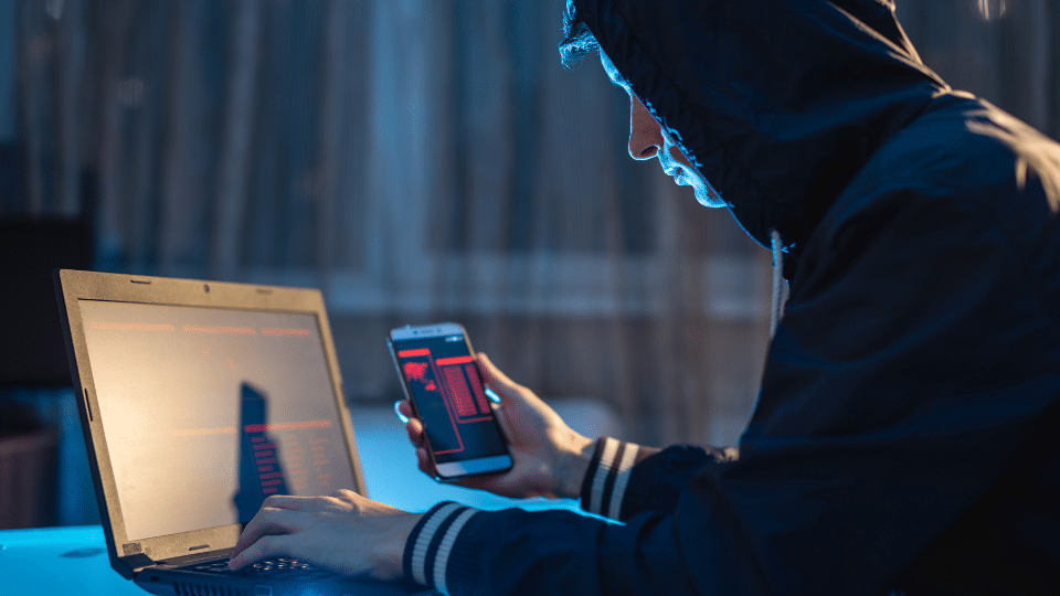 Man with hood hacks mobile phone on computer