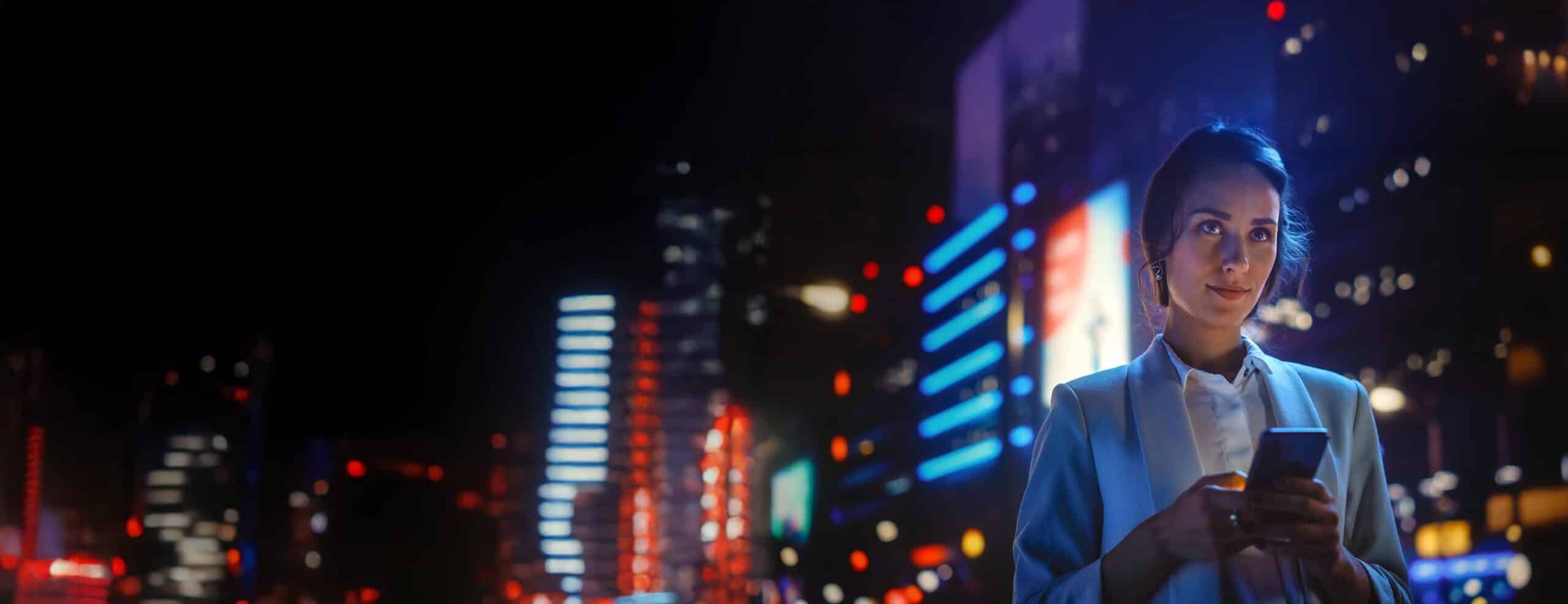 Beautiful Young Woman Using Smartphone Standing on the Night Cit