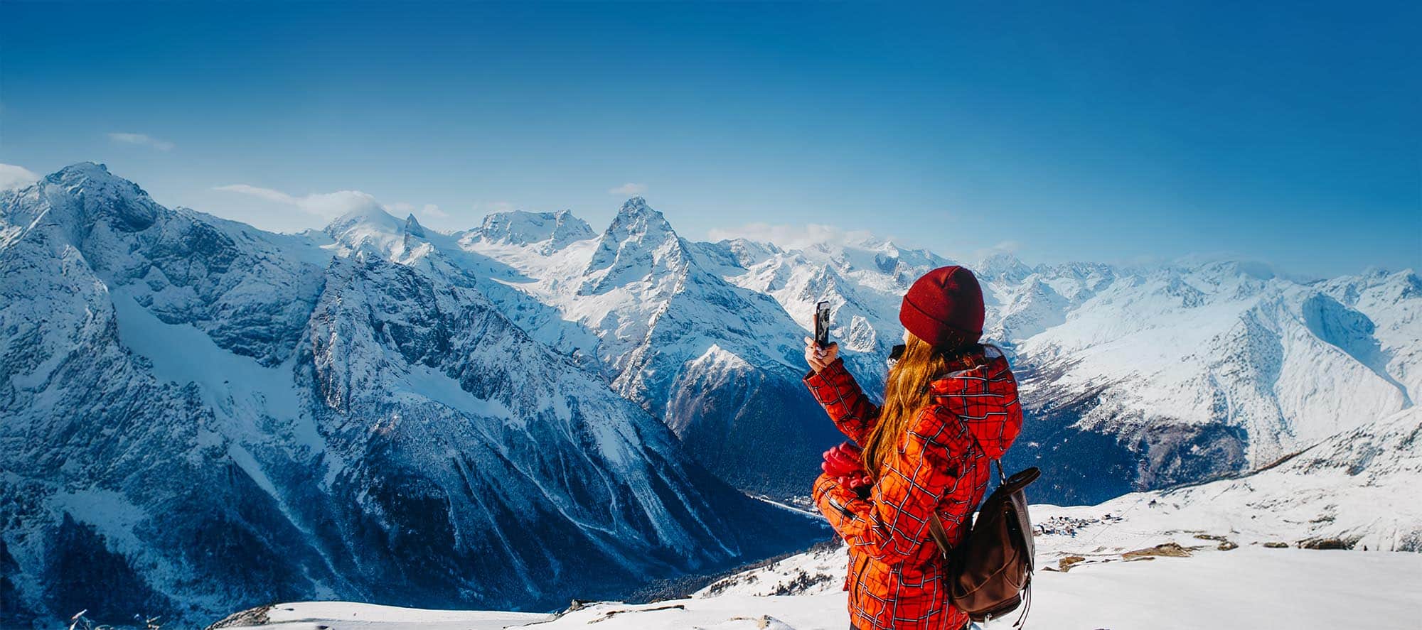 A woman with a backpack takes pictures in the mountains in winte
